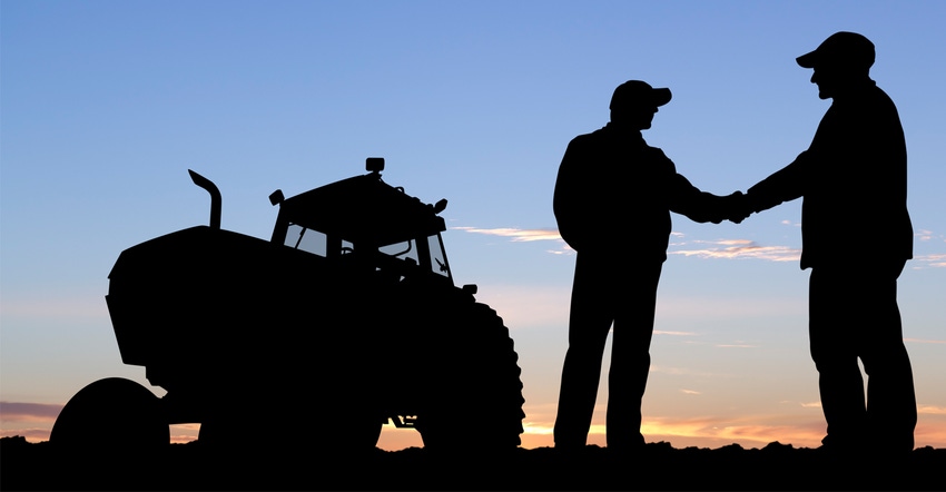 Farmers shaking hands next to tractor during sunset