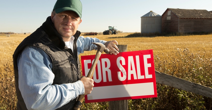 A farmer nails a 'For Sale' sign on his fence