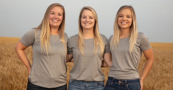 Three young women stand together to pose in the middle of a field