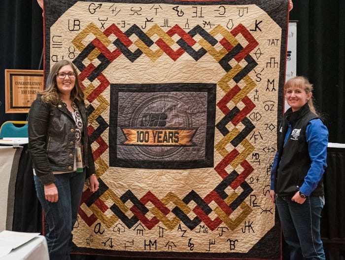 Converse County Rancher Rachel Grant stands next to a quilt handmade by Niobrara County Rancher/WyFB YF&R Committee Member Chelsea Baars