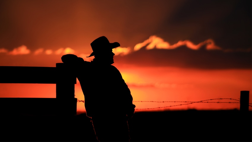 silhouette of farmer leaning on fencepost during sunset