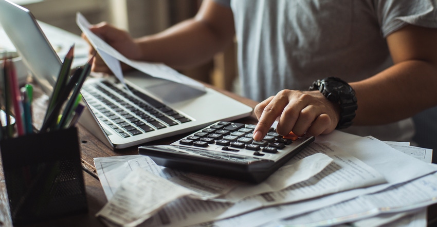 person using calculator while sitting at desk holding papers