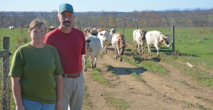 Roy and Jen Coale standing in front of a herd of cattle out in the pasture Roy and Jen Coale standing in front of a herd of cattle out in the pasture