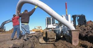 Two men installing a tile drainage system next to a field