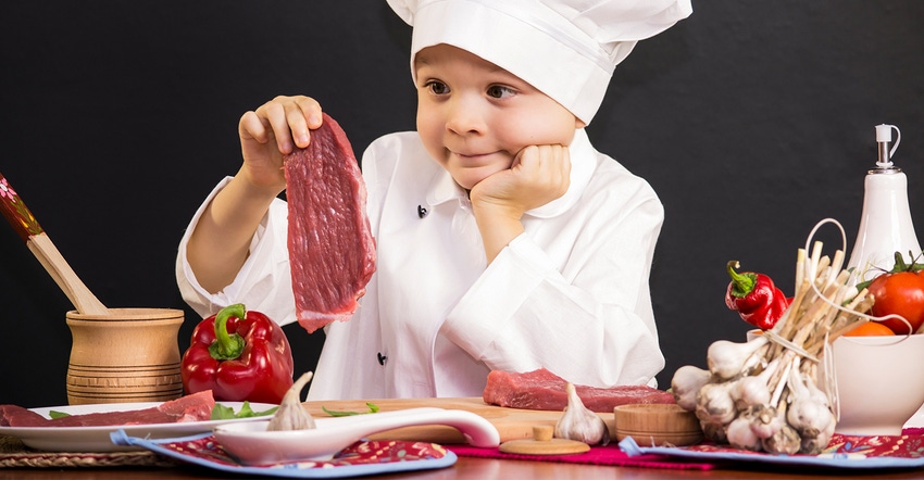 child in chef's hat holding up red meat