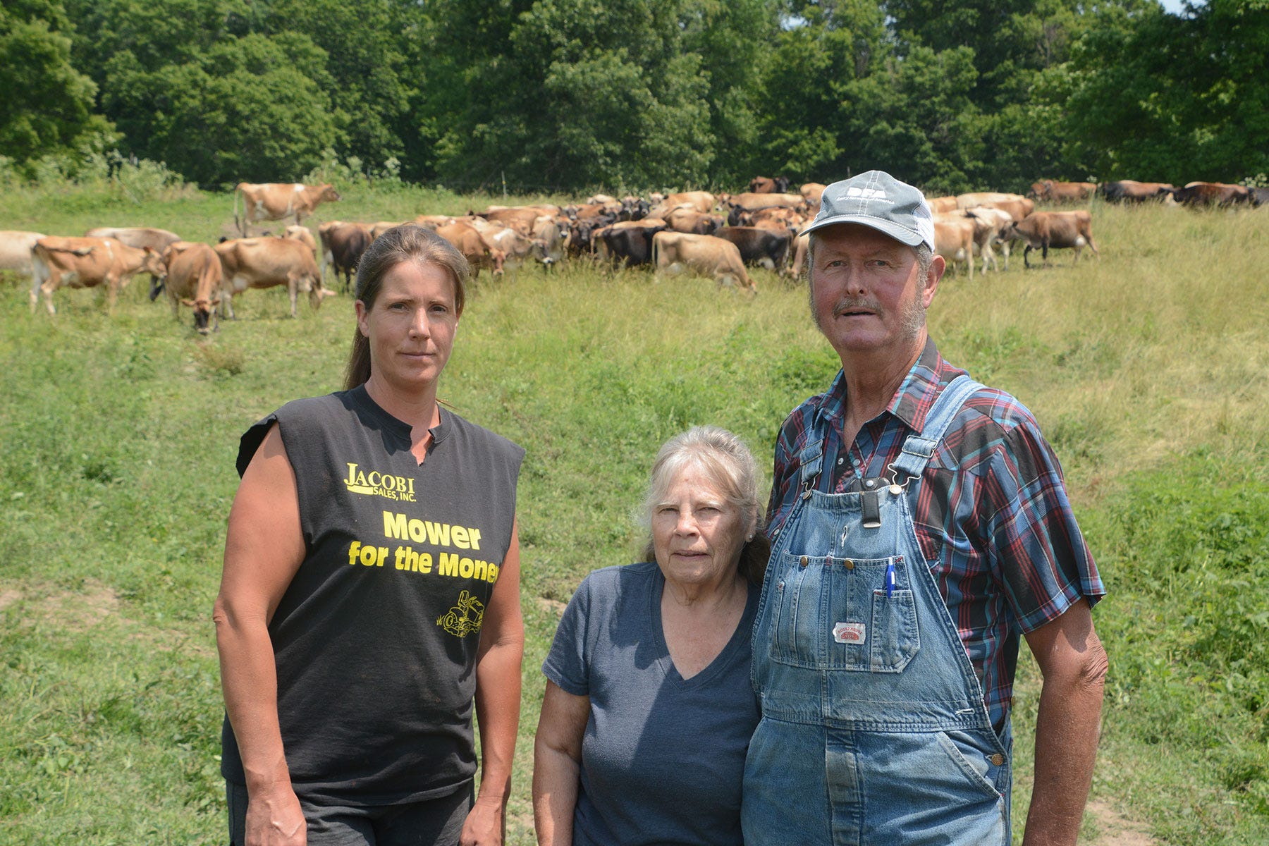 Sarah, Judy and Mike Ponsford stand in a pasture with a herd of Jersey cows behind them