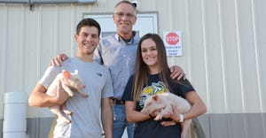 Karl Schenk and his children, Karl II and Kyra, stand in front of their nursery barn holding piglets