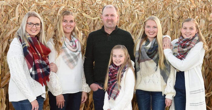 A couple with their four daughters pose in front of a corn field