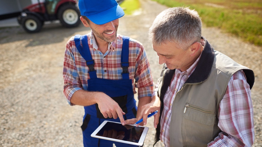Two men on a farm looking at an tablet.