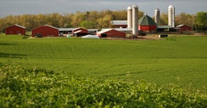 multiple red farm buildings in the distance of a lush green field