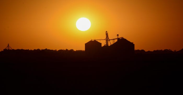 An orange sunset behind grain bins An orange sunset behind grain bins