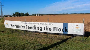  A banner that reads Farmers Feeding the Flock, displayed in front of a crop field