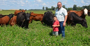 Andy Lohr with his grandson, Eli standing in front of herd of grazing beef cattle