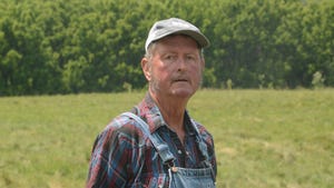 A close-up of a farmer standing in a green pasture