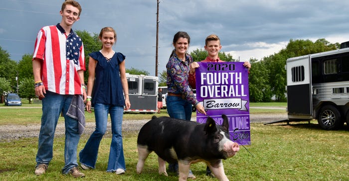 Nate and Ella Kavicky and Ashley and Zach Strueh, who is holding a big purple banner, pose with black barrow hog 