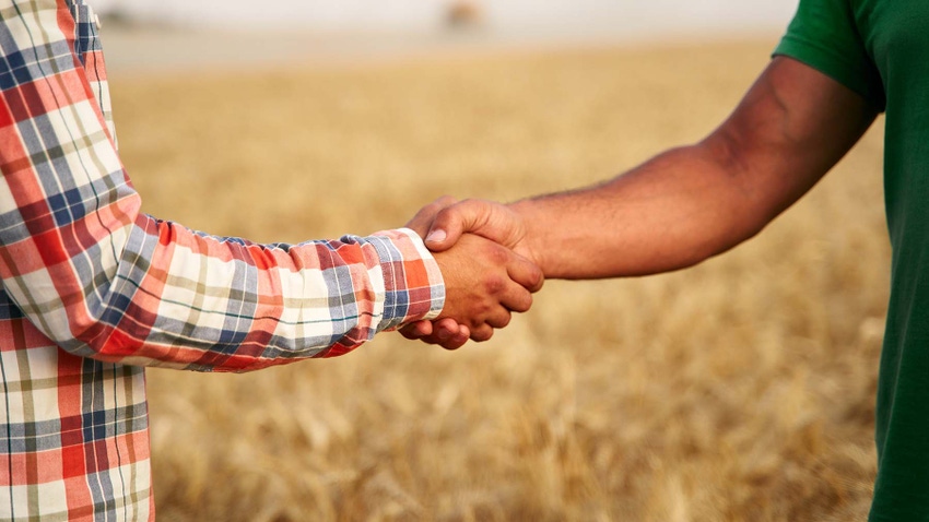 Two people shaking hands in a farm field