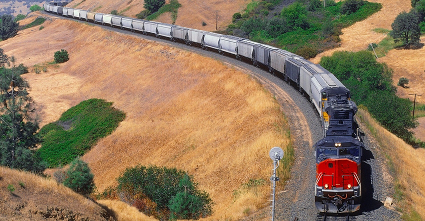 A loaded grain train hauled by two diesel-electric locomotives winds its way round a curving hillside embankment on the way f