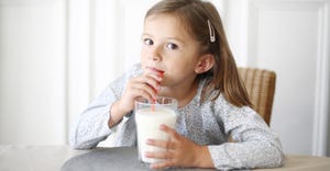 Young girl sitting and drinking milk out of a glass and straw