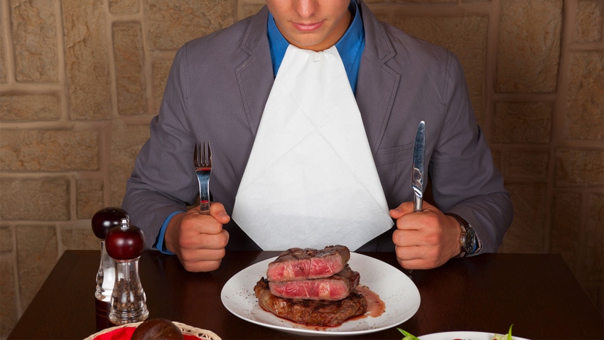 Man with eating utensils sitting at a table with a medium rare steak plated in front of him