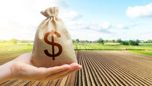 A hand holding a bag of money with farm field in background
