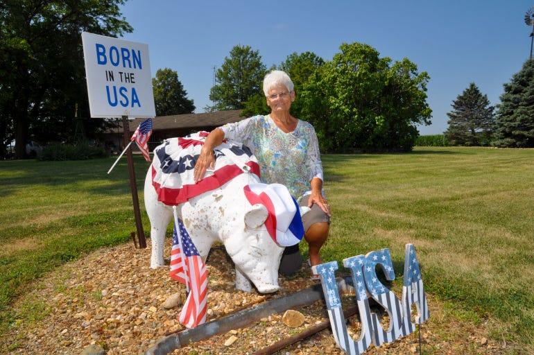 Sandy Nelson kneels beside s a concrete pig in her front yard decorated for the Fourth of July