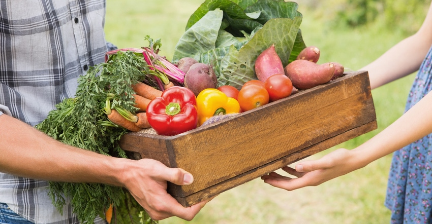 farmer handing box of vegetables to customer
