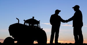 Farmers shaking hands in field during sunset