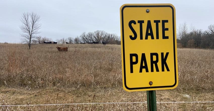 yellow "State Park" sign with cattle grazing in brown grass in background