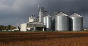 grain bins by brown soybean field