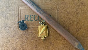  A golden charm positioned next to a pencil and metal pin on a leather background