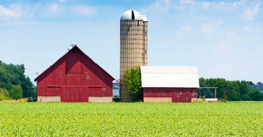 A red wooden barn and tall silos behind a field