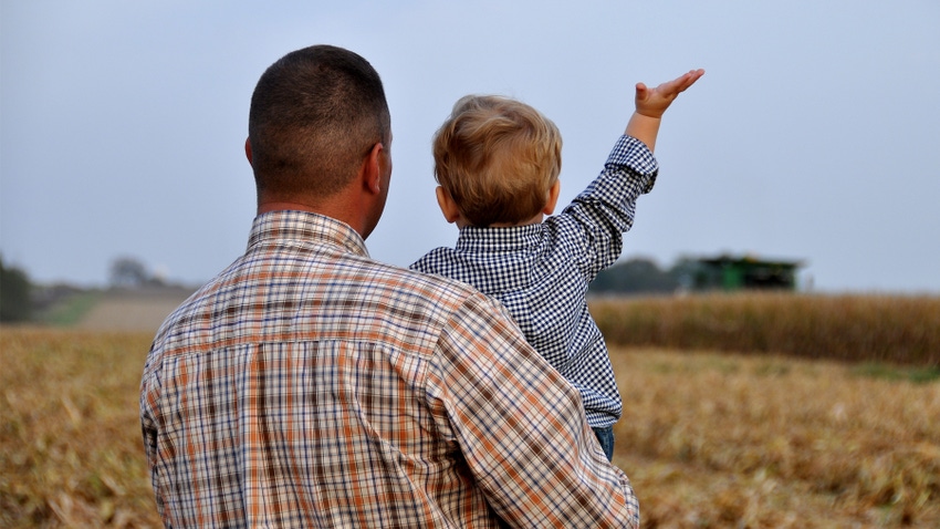 father holding son watching harvesting of corn