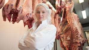 Woman with pork and beef carcasses in meat locker