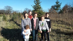 Family posed in front of a Christmas tree at a tree farm.