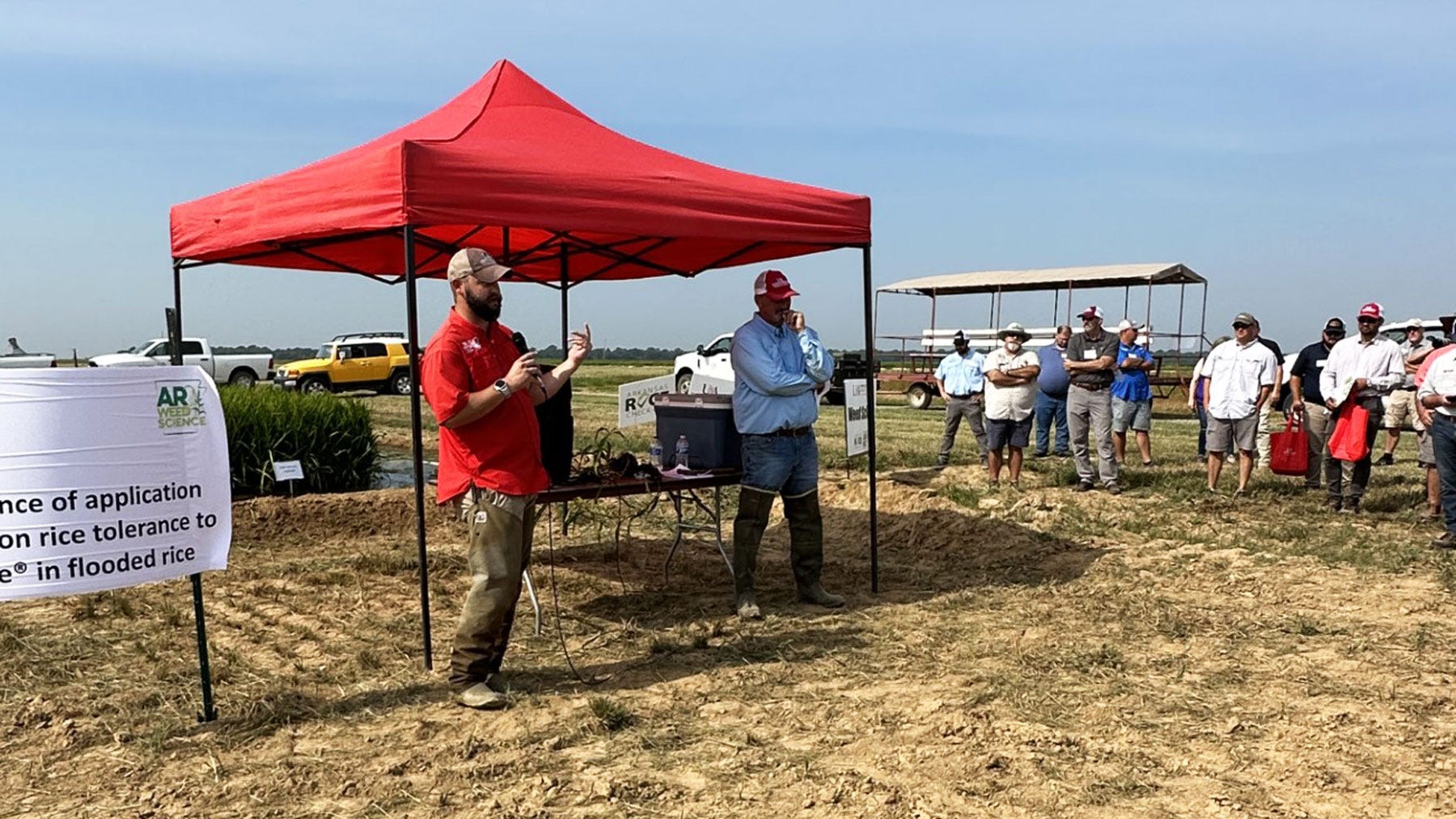 Two men presenting at field day under red tent to a group of attendees. Photo by Whitney Haigwood