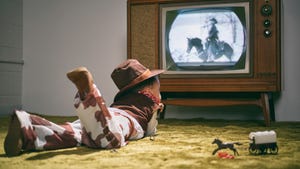 little boy dressed as cowboy laying on carpet in front of black and white TV