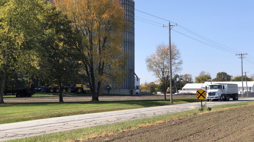 truck driving down rural road in front of grain bin and elevator