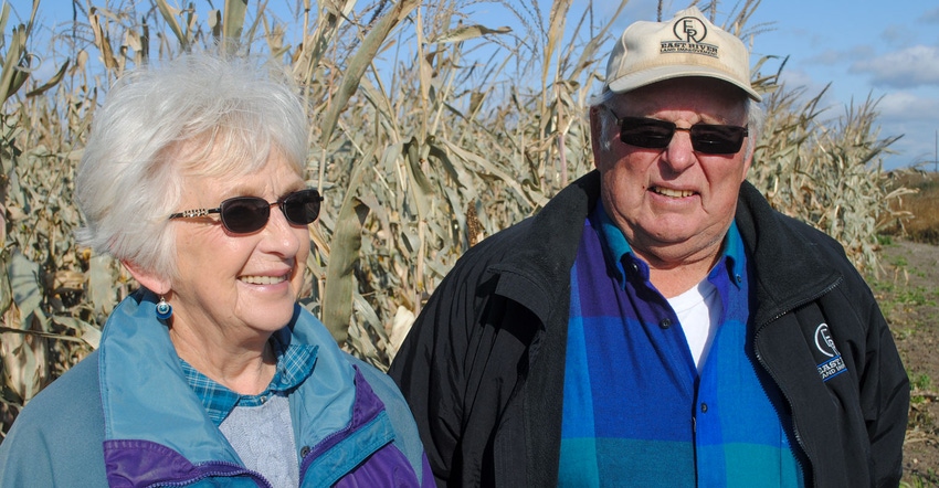 A close up of an older man and woman standing in front of a tall crop and smiling