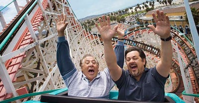 Two men riding a roller coaster with their hands in the air.