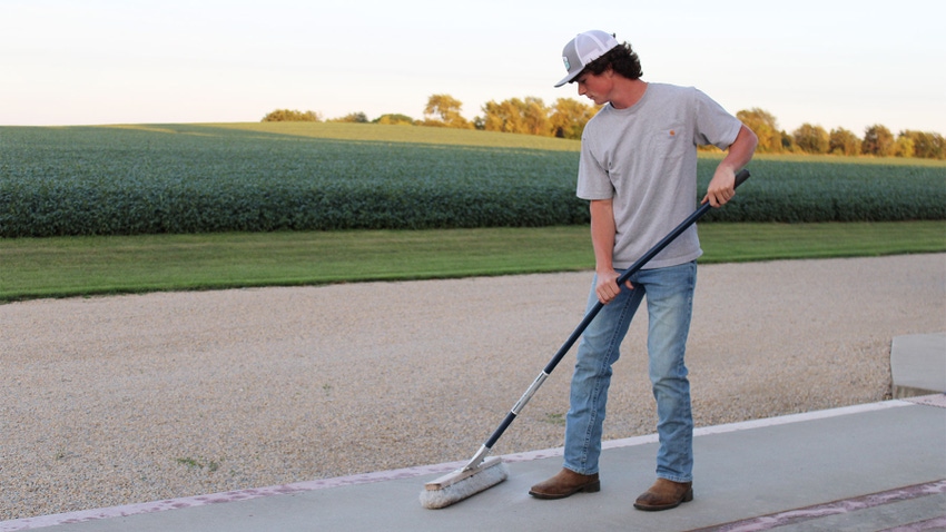 A young man sweeping a concrete platform and a field in the background