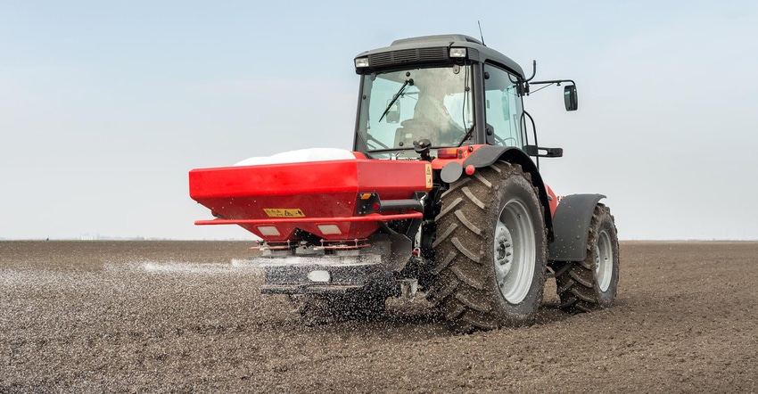A red tractor spreading fertilizer on a bare ground