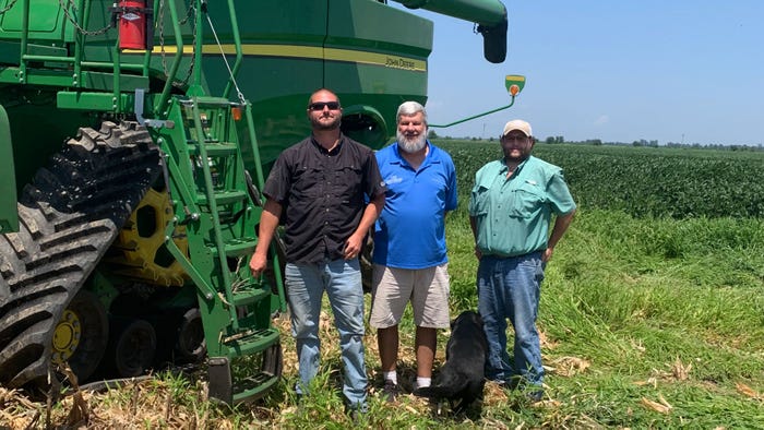 Three men standing in a field next to a green combine.