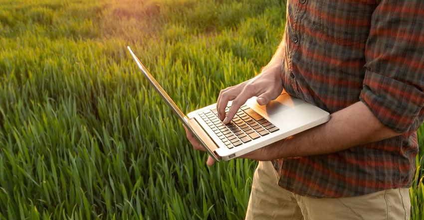 A close up of a male farmer typing on a laptop in a field