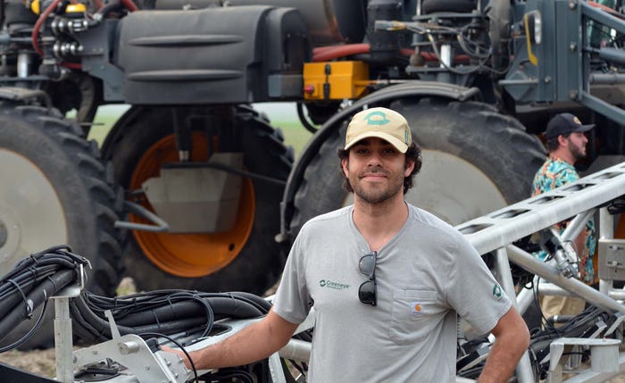 Man with hat posed next to large agricultural sprayer