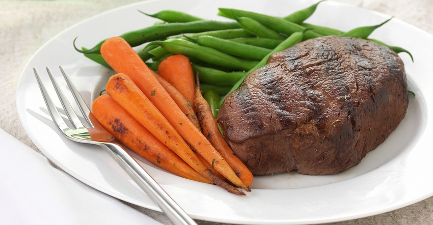 A steak served on a white plate with carrots and green beans
