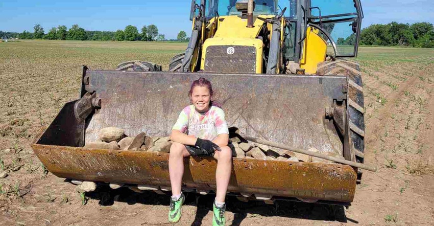 Girl sitting in the bucket of a loader with rocks