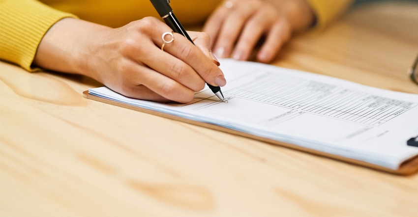 Closeup shot of an unrecognizable woman filling in paperwork on a clipboard at a table