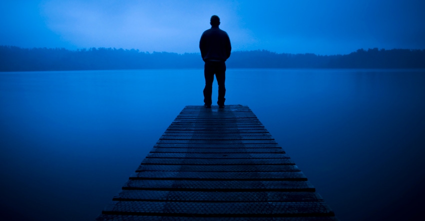 silhouette of a man standing on a pier looking out over a lake