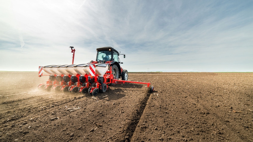 A farmer in a tractor seeding a field of soil
