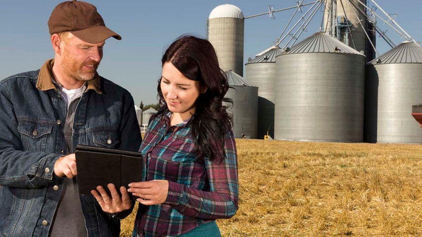 Man and woman talking looking at tablet with farm in background.